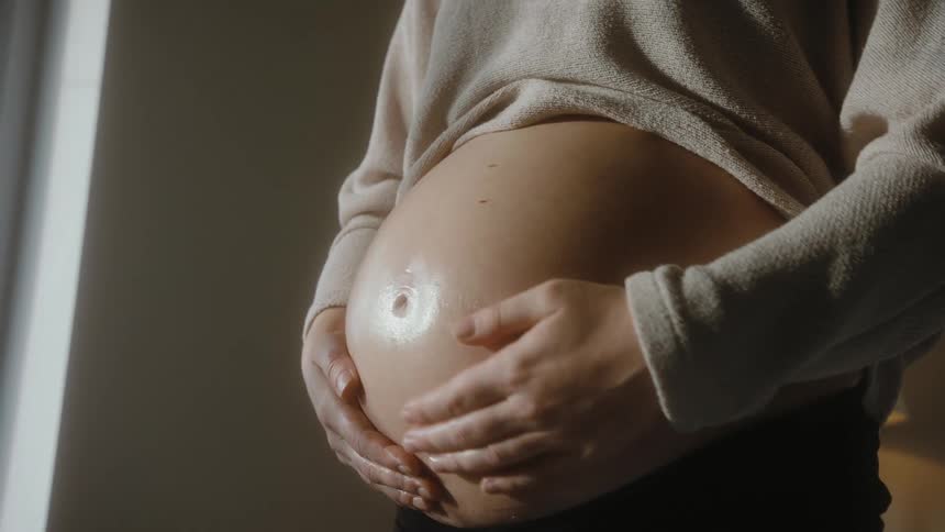 Pregnant woman rubs her belly with oil