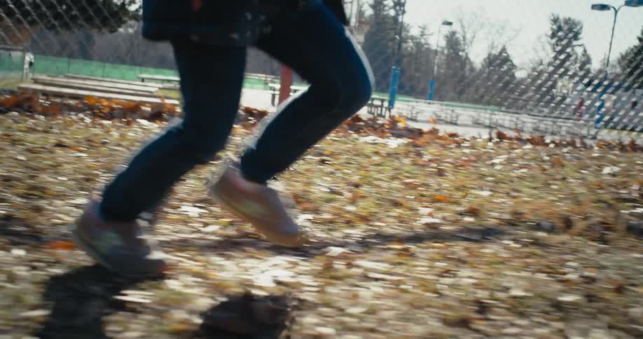 Two people run on the leaf covered ground in the park