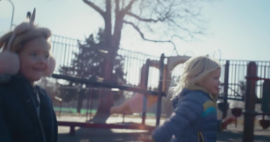 A pair of young girls run across a playground during the day