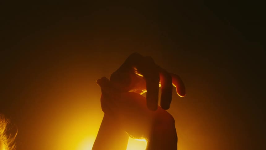 A dancer moves her hands gracefully while posing before a stage light in a dark place