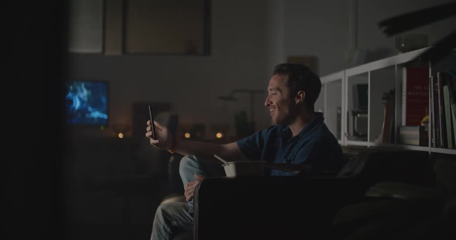 Man with blue shirt jeans sits on couch and makes video call