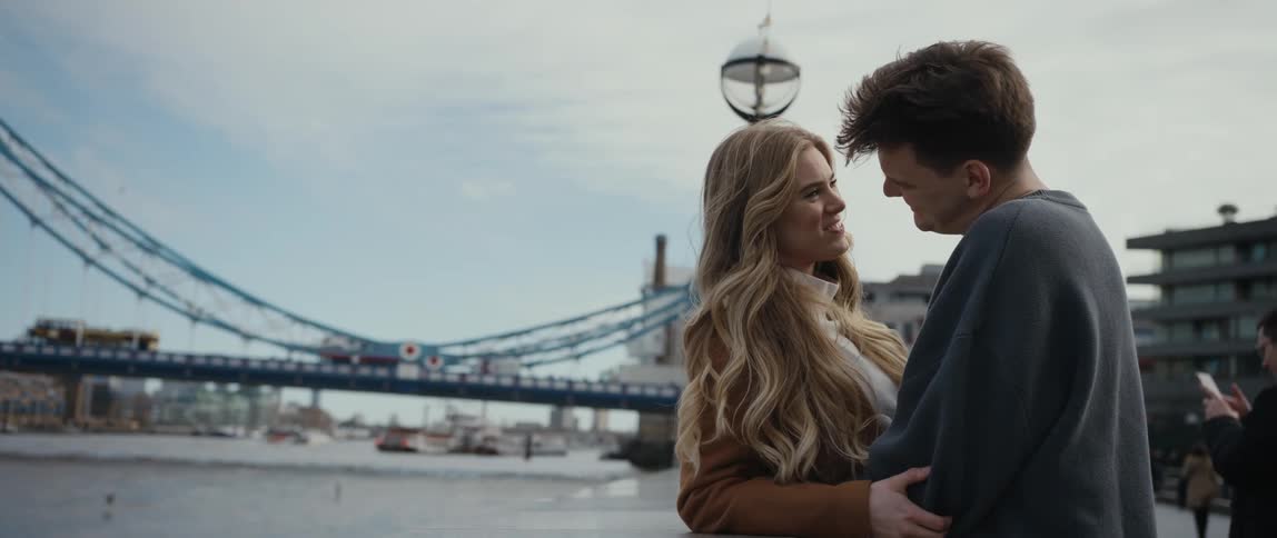 Man and woman embrace as the man kisses the woman on the forehead while standing near the river