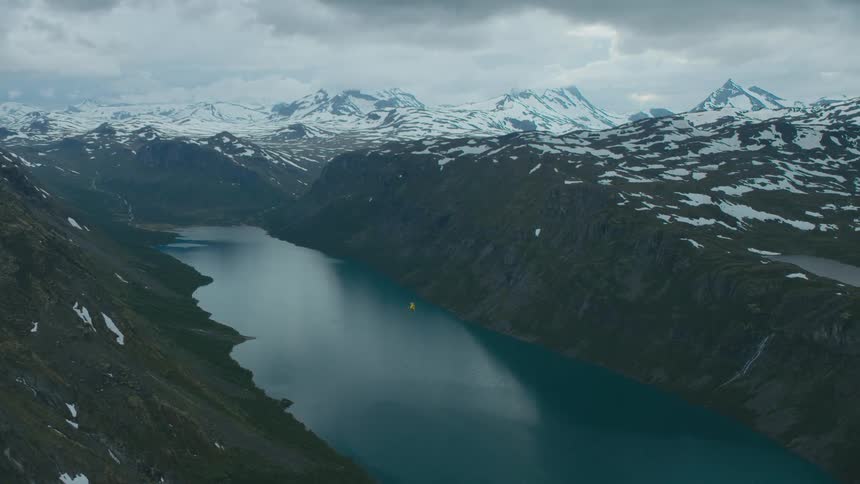 A helicopter flies over a river in a mountain valley on a cloudy day
