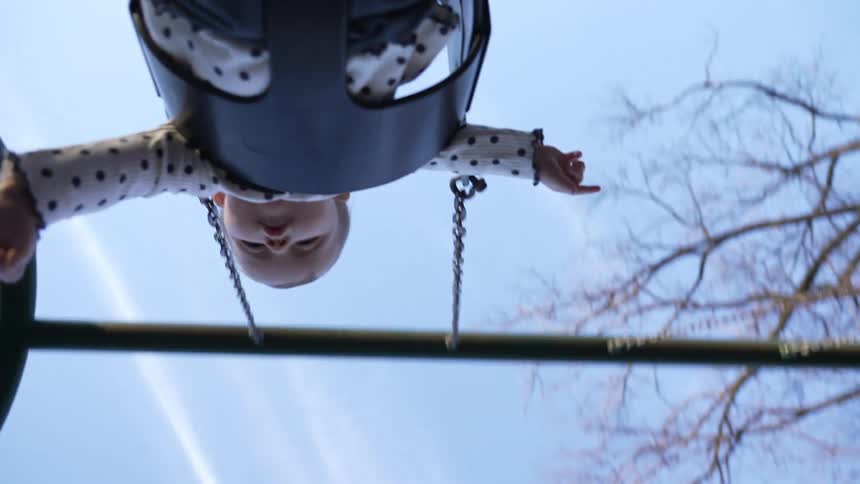Baby sitting in a fullbucket swing seat and swinging in an outdoor playground