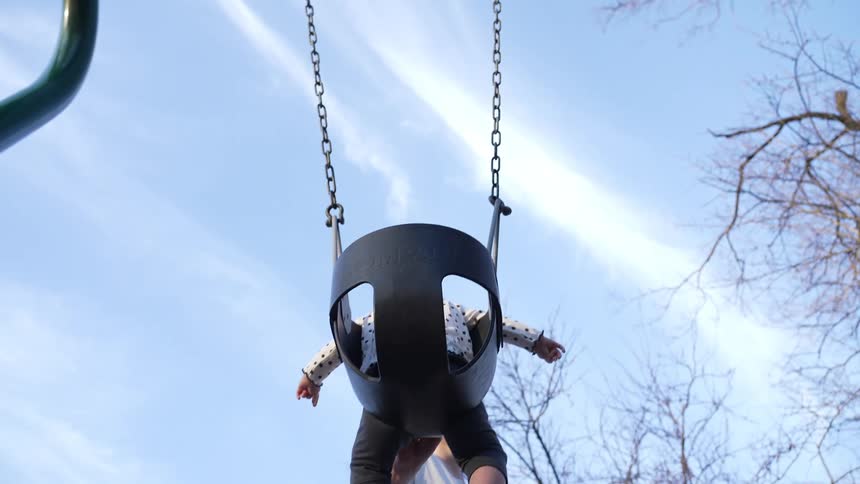 A woman pushes her daughter on a swing in the park