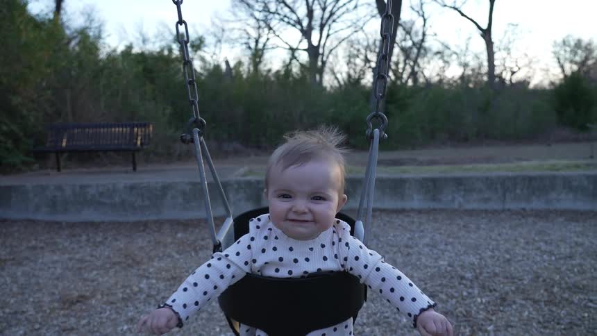 Happy baby swinging in a bucket swing at the park