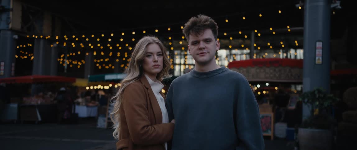 A woman holds the arm of a man as they look into the camera while standing outdoors during the day