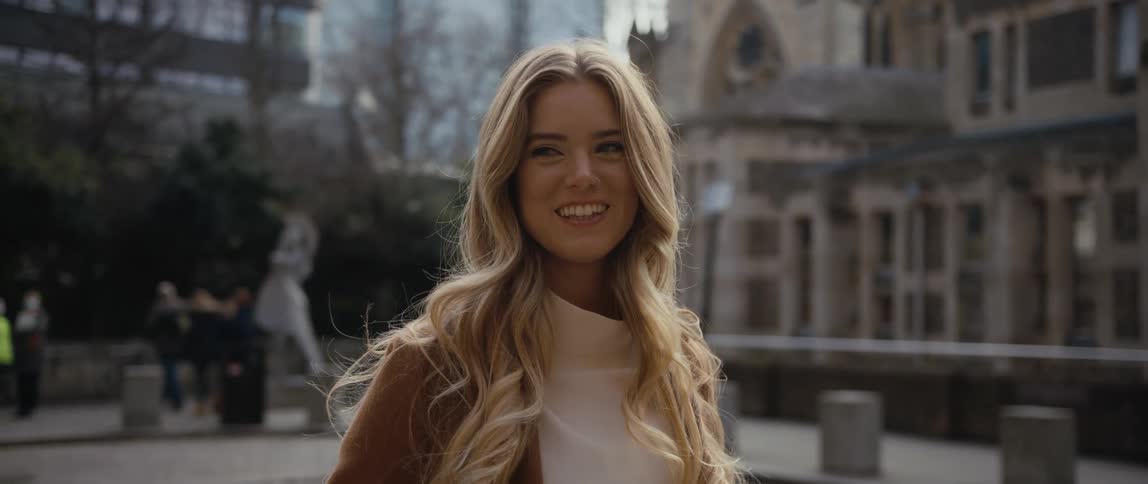 A woman stands in the street and smiles as people walk behind her