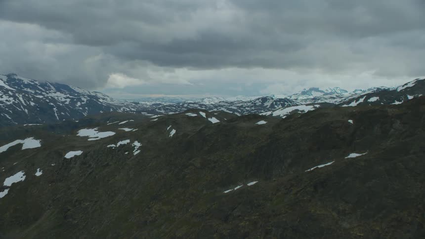 Mountains become more dappled with snow as they near the horizon under an overcast sky