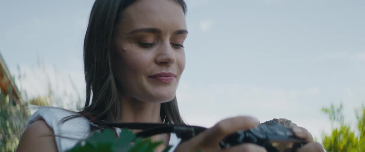 Woman standing outdoors using her photography camera to take pictures of some plants at a sunny day