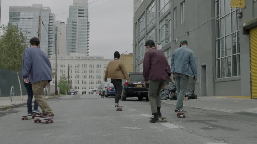 Five people are skateboarding down a city street