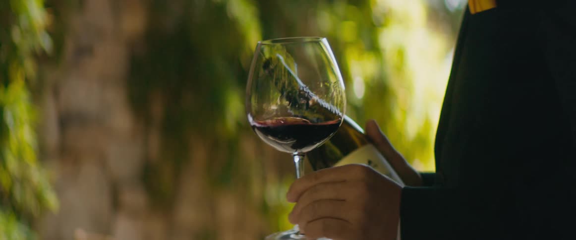 Waiter holding a wine bottle and serving a glass wine to a woman sitting at a restaurant table