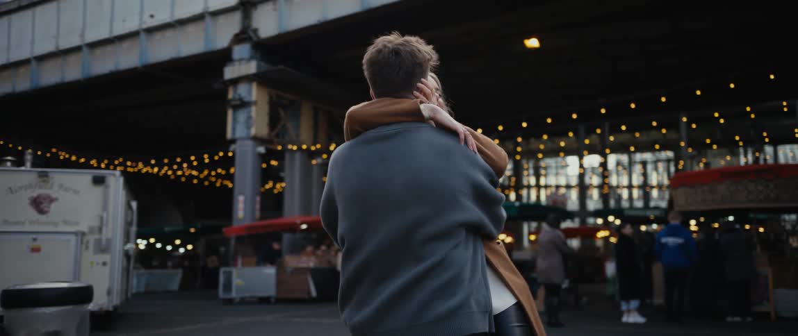 Two teenagers walk away from outdoor shops and spin around and hug one another and kiss