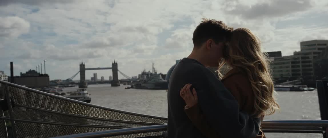Man and woman standing at the balcony hugging and kissing each other while enjoying the view of the river ahead at a big city