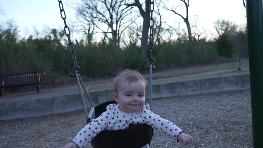 Happy baby swings in swing in playground at dusk