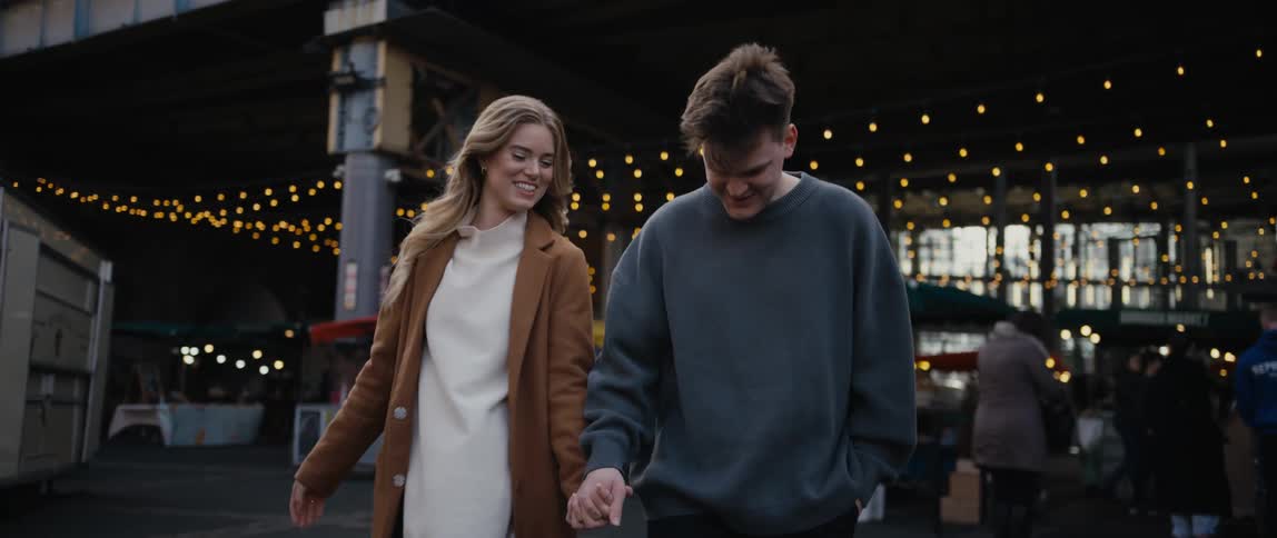 Man and woman romantically walking while holding hands and kissing near a street fair in the city