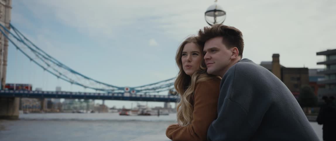 Man hugging a woman from behind while theyre standing in front of a river enjoying the view ahead