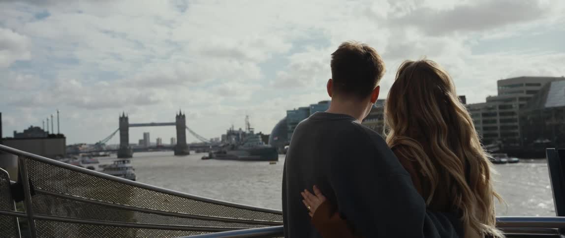 Man and woman hugging and standing at the balcony looking to the view of a river and bridge ahead