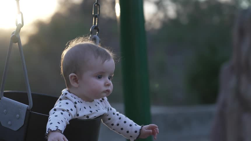 Mother swings baby in swing in playground at dusk