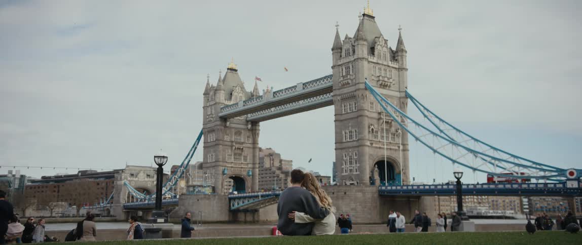 Man and woman sitting together hugging and kissing each other while looking at the view of the river and bridge ahead