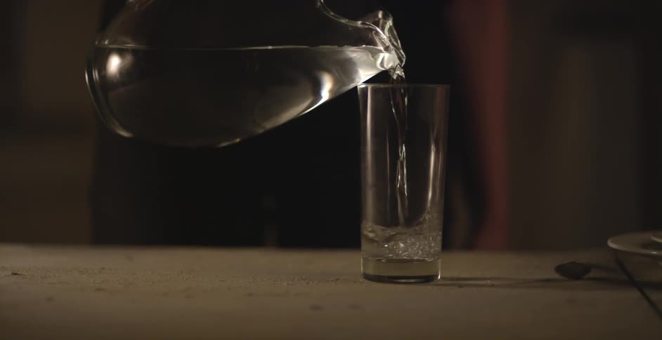 Water being poured into a tall glass from a clear pitcher