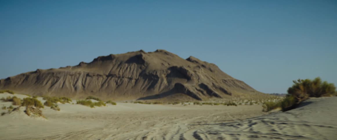Tire tracks leading away from a mountain in the desert during the day
