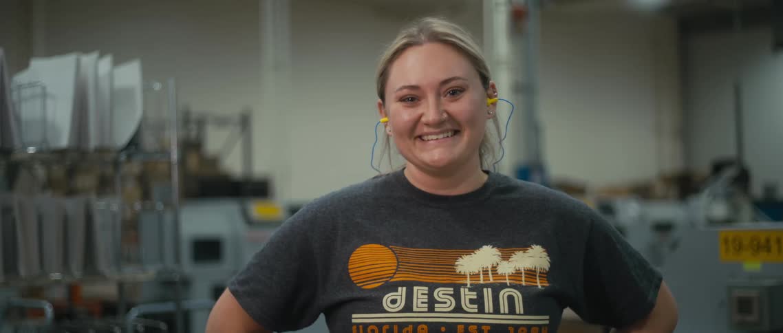 A woman wearing earbuds smiles into the camera while standing indoors