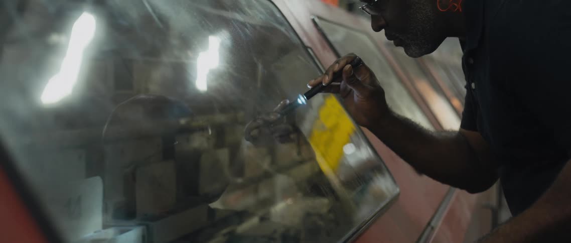 A man shines a small flashlight on a television screen showing video of stadium seating