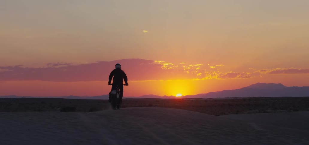 Male biker with helmet riding dirt bike is silhouetted against the sunset in the desert
