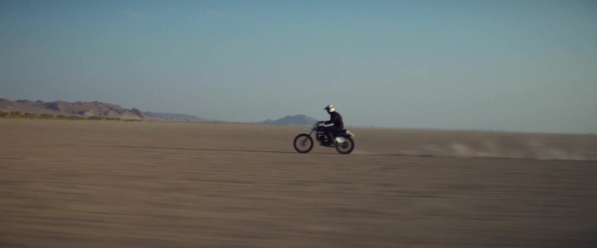 Male biker with white helmet and black jacket rides dirt bike in the desert
