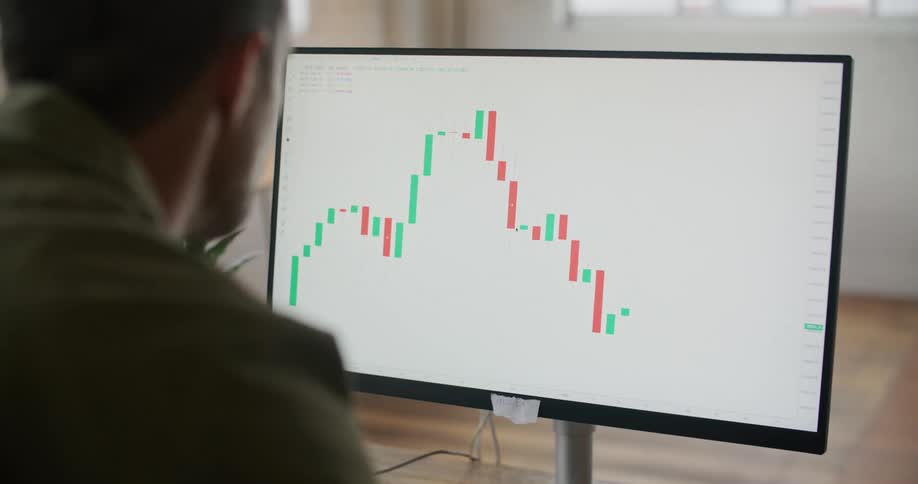 A man is sitting at a desk looking at a monitor with a graph on the screen