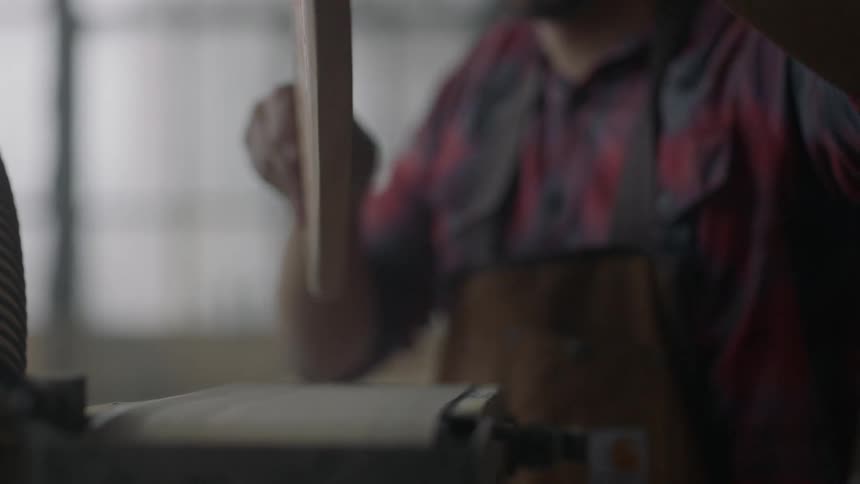 A man shapes a piece of wood on a sanding belt