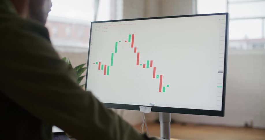 A man is sitting at a desk looking at a monitor with a graph on the screen