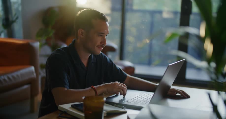 Man with mustache blue shirt wristband and wristwatch opens and works on laptop at coffee table