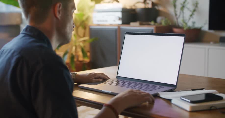 A man is sitting in front of a laptop computer with a white screen