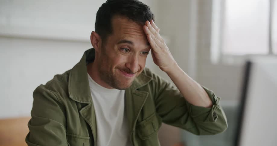 A man is sitting down at a desk holding a computer mouse and looking at the monitor