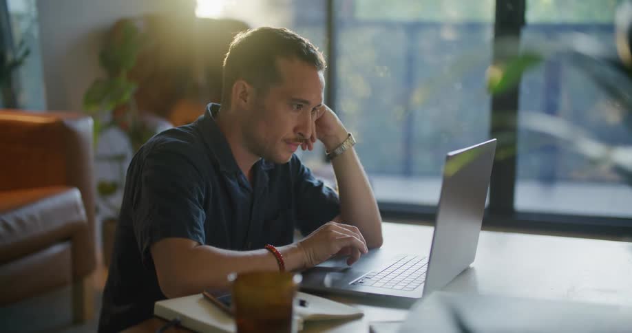 A man writes in a book and types on his laptop as he works