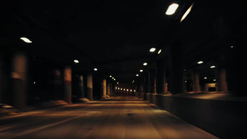 A dark tunnel at night with a car driving in it as seen from inside a vehicle