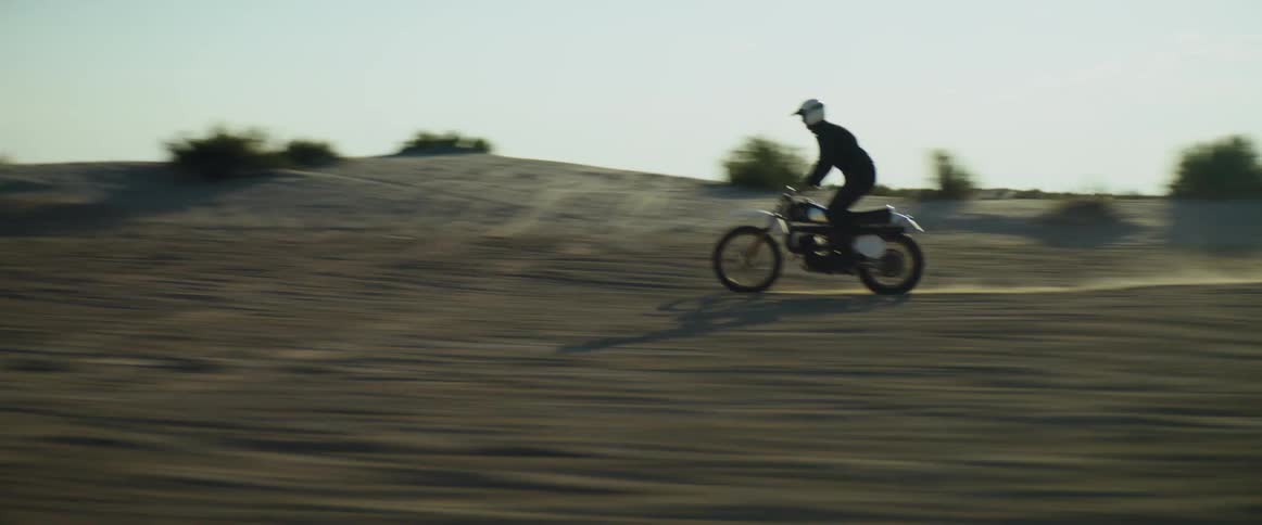 A person rides a motorcycle through an arid hilly countryside on a clear day