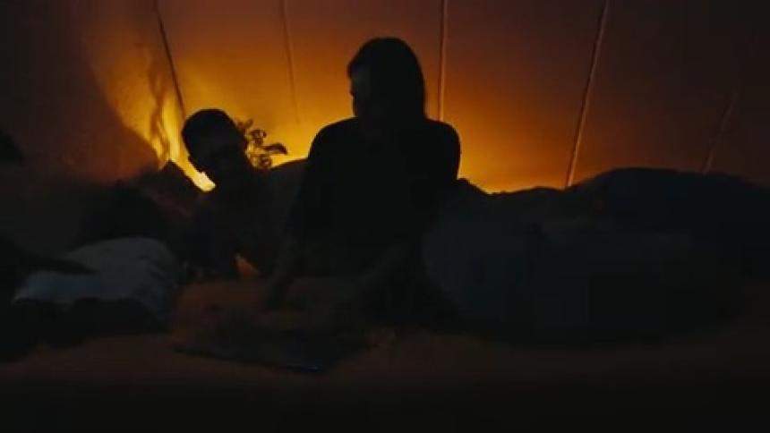 Woman sets a laptop next to her in bed then turns to her husband and they snuggle