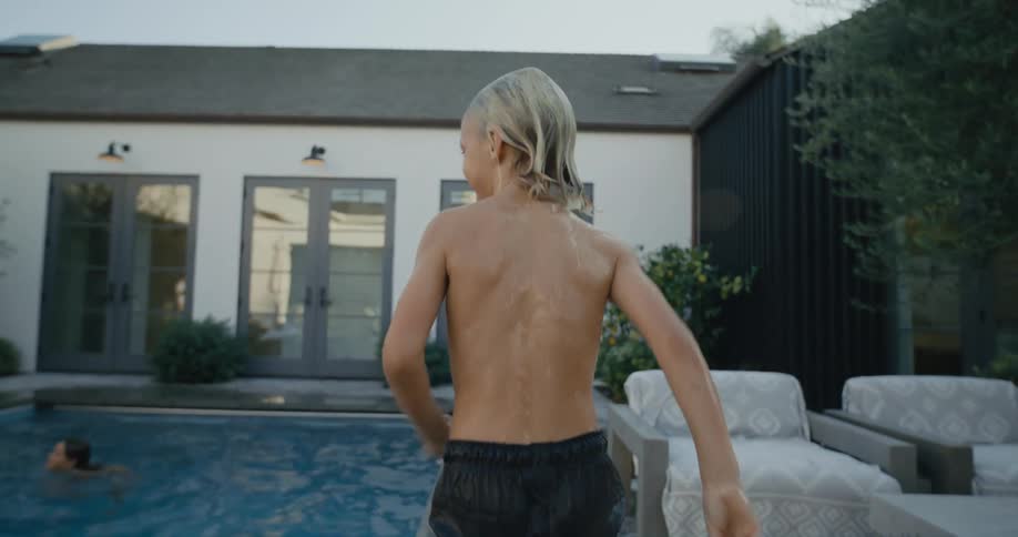 Boy runs along side of pool as family plays in water