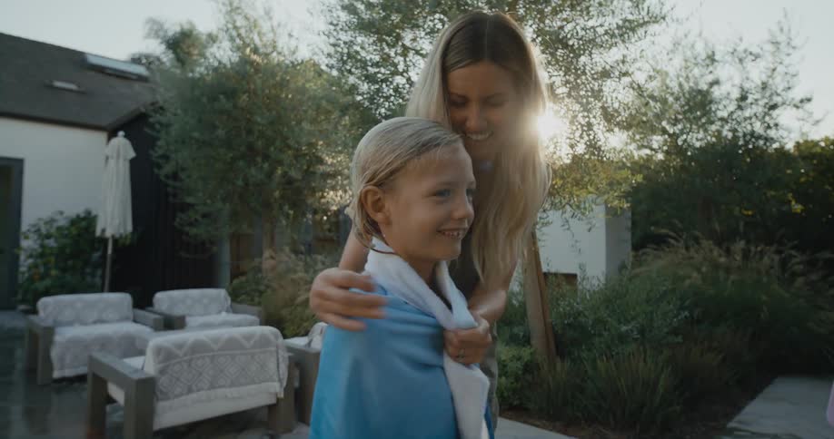 Boy leaves the pool and his mother wraps him with a towel and hugs him