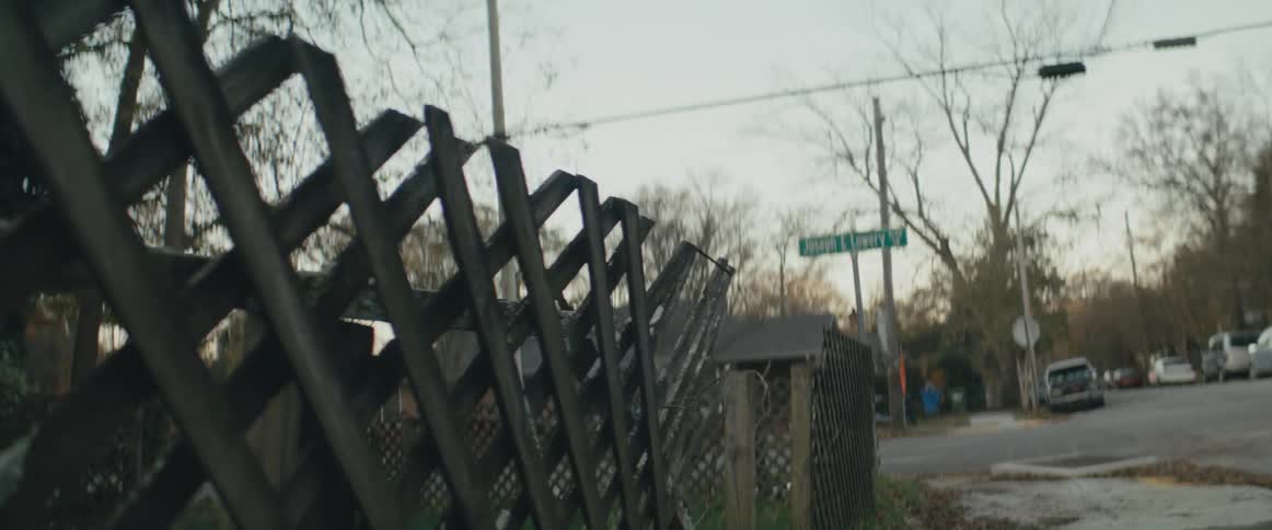 A fence that is falling apart in a neighborhood on a street with cars