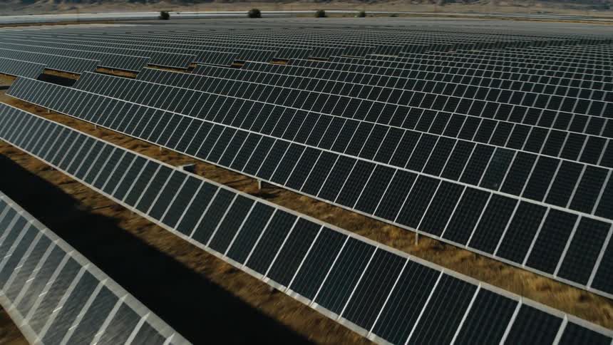 Sunlight shines on solar panels on a solar farm with mountains in the distance