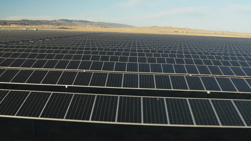 Sunlight shines on solar panels on a solar farm with mountains in the distance