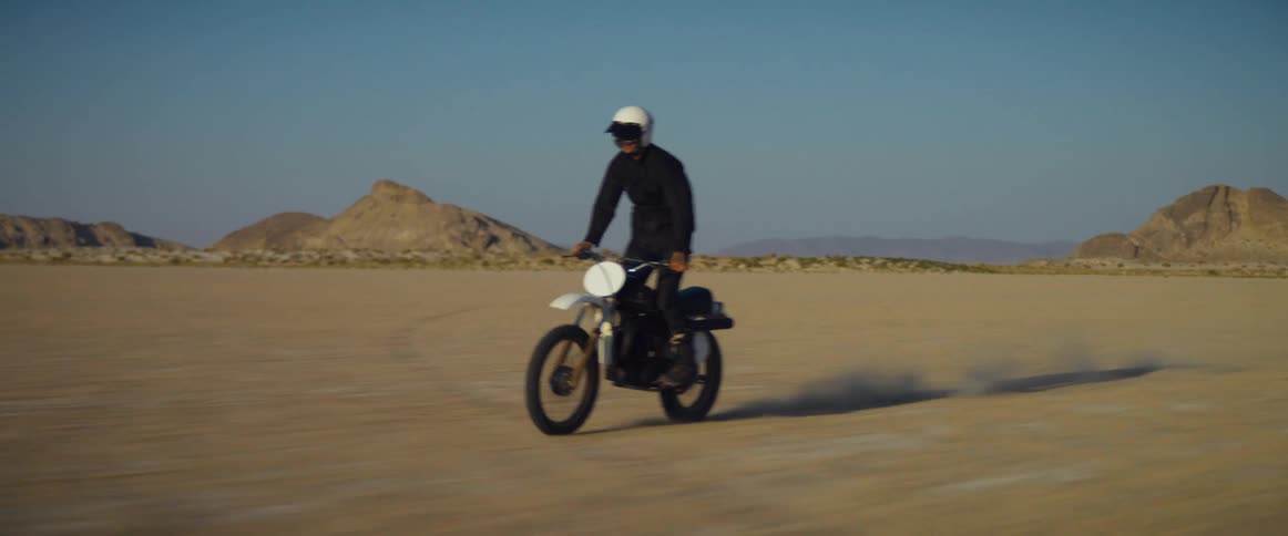 Motorcycle rider rides a motorcycle through the desert in a stand up position under a blue sky