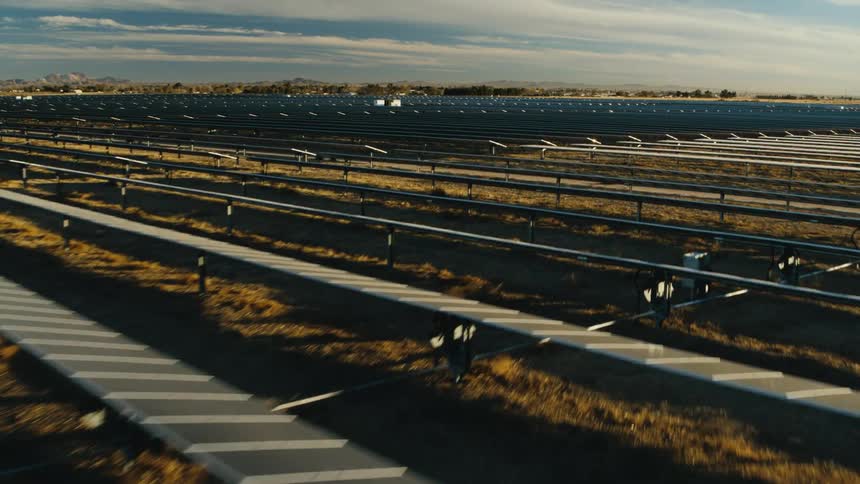 Sunlight shines on solar panels on a solar farm with mountains in the distance