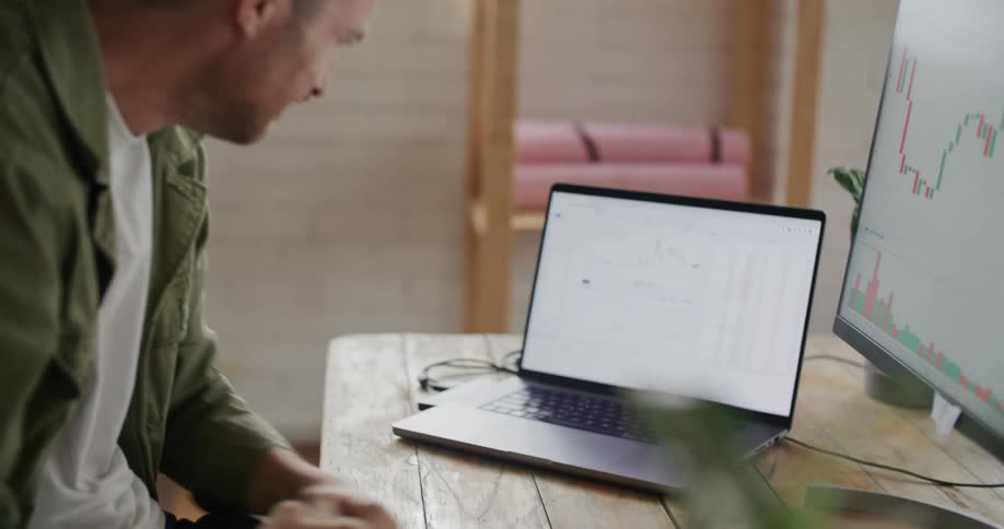 A man cries and strikes the table while looking at a price by volume chart on a laptop