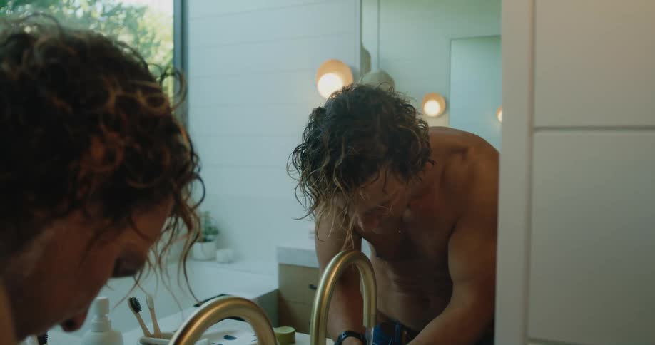 Shirtless man with wavy hair freshens up in bathroom