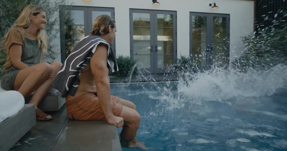 Siblings jumping into swimming pool as parents watch poolside